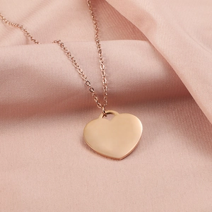 Close-up of a polished rose gold heart pendant on a fine chain over pink silk fabric