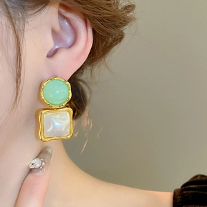 Detail of mint green resin and pearl square earring on ear with gold wavy edge