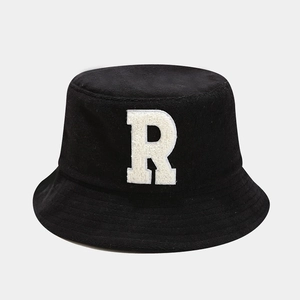 Close-up of black bucket hat featuring a white fuzzy letter R patch and stitched brim