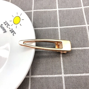 Close-up of a hollow gold duckbill hair clip on a white plate with grey grid background