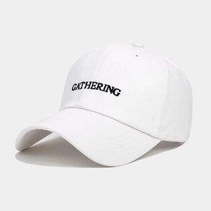 Detail of white cotton baseball cap showing black GATHERING embroidery and twill texture