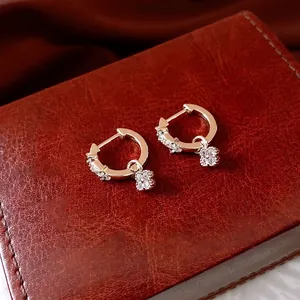 Boucles d'oreilles créoles fleurs dorées avec zircons sur un écrin à bijoux en cuir chic