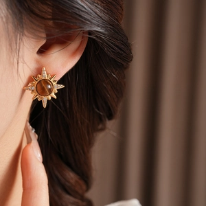 Macro detail of gold starburst earrings with brown tiger eye stone on model ear
