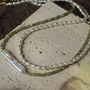 Detail of baroque pearl necklace with olive green zircon beads on beige travertine stone