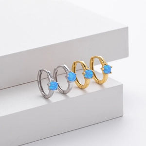 Detail view of gold and silver hoop earrings with blue opal stones on white geometric stand