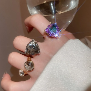 Macro shot of rose gold rings with colorful triangular gemstones on hands holding a glass