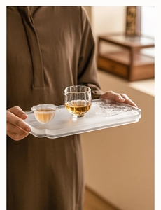 Close-up of a person holding a crystal glass tea tray with a pitcher and small tea cup