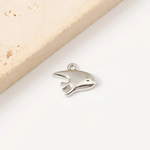 Detailed view of a silver fish-shaped stainless steel pendant on a beige stone