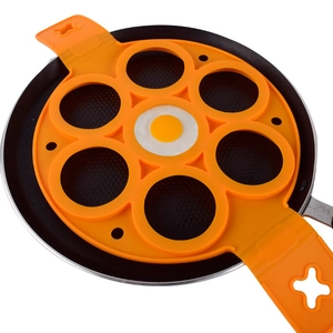 Top view of an orange 7-hole silicone pancake mold with a fried egg on a black frying pan