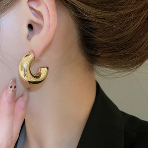Close-up of a model wearing minimalist thick C-shaped golden earrings with a glossy finish