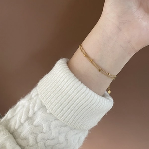 Detailed close-up of double-layer gold beaded bracelet on a white tweed sleeve