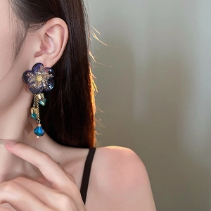 Detailed view of blue flower tassel earrings with gold bead accents on a model
