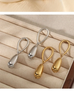Close-up of polished teardrop earrings in gold and silver finish on a soft fabric base