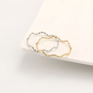 Set of two minimalist wavy stackable rings in gold and silver finish on ceramic tray