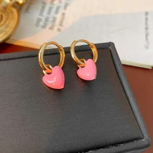 Close-up of pink heart-shaped enamel drop earrings on a black textured jewelry box