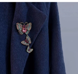 Detailed butterfly brooch with turquoise beads and pink crystals pinned on a navy wool coat