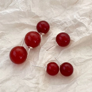 Flat lay of multiple sizes of red agate stud earrings on textured beige paper background