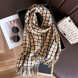 Detail of soft yellow and black plaid scarf with fringe on a tray with accessories