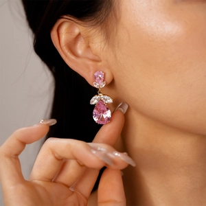 Gros plan de boucles d'oreilles gouttes en zircon rose et fleurs dorées sur modèle