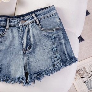 Dettaglio di pantaloncini in denim azzurro strappati con orli sfrangiati su pelliccia bianca