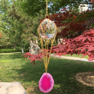Close-up of a faceted crystal ball with pink agate slice hanging in a sunny autumn garden