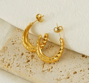 Detail view of 18K gold plated twisted C-shape hoop earrings on a beige textured stone