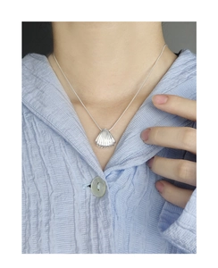 Detail of silver shell pendant on a snake chain necklace worn on light blue shirt