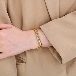 Close-up of a gold 3D heart-shaped link bracelet worn on a wrist with a beige suit