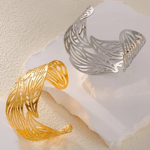 Minimalist gold and silver leaf feather open bangles on a textured stone surface