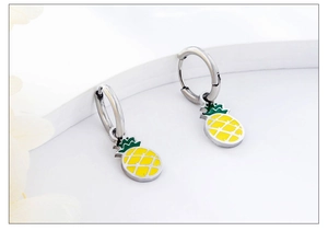 Close-up of yellow pineapple charm earrings with green leaves and silver metal hoops