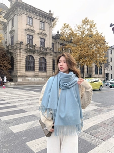 Close-up of a light blue thick scarf with fringe detail worn by a model in the city