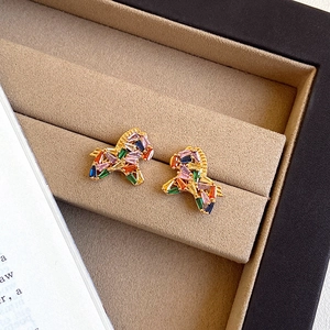 Macro detail of gold horse stud earrings with colorful cubic zirconia on velvet