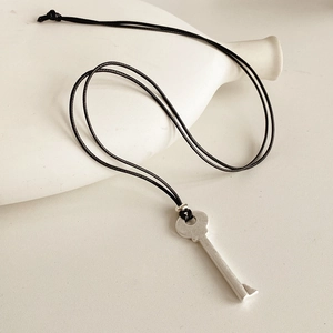 Détail du pendentif clé argent mat sur cordon noir contre un support en céramique