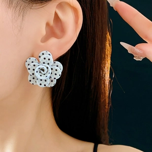 Gros plan de boucles d'oreilles fleurs en acrylique bleu à pois noirs sur un modèle