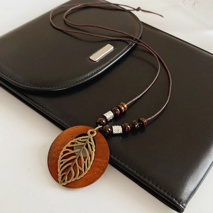 Détail du pendentif en bois avec feuille de métal ajourée sur cordon en cuir