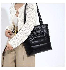 Detailed view of black quilted puffer tote bag worn by model in minimalist winter outfit