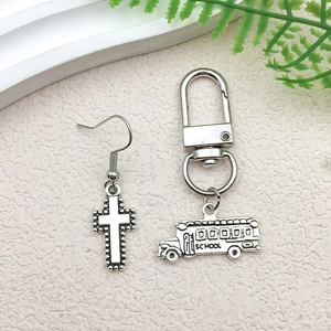 Silver alloy charms featuring cross earrings and school bus keychain on textured surface