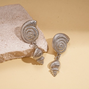 Macro detail of silver seashell earrings with spiral textures on natural stone background