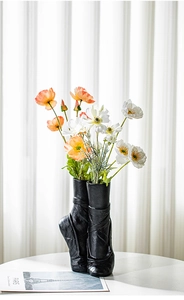 Detail von Ballettschuh-Keramikvasen mit orange-weißen Blumen vor weißem Vorhang