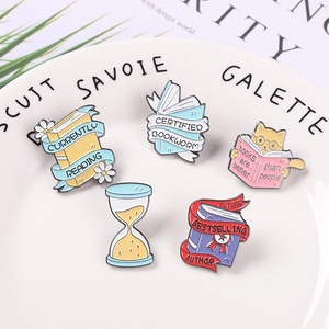 Five-piece set of colorful book and cat themed enamel pins on a white ceramic plate