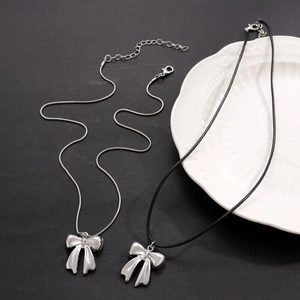 Bow pendant necklaces with silver snake chain and black cord styles on a ceramic tray