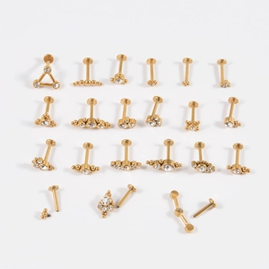 Set of gold-plated 16G piercing jewelry with white crystals on a white background