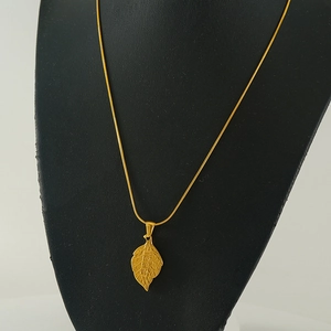 Detailed view of a gold titanium steel necklace with an engraved leaf pendant on a mannequin