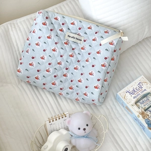Detail of light blue floral quilted makeup bag with zipper and logo patch