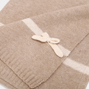 Macro shot of knitted camel scarf featuring a soft bow detail and white stripe texture