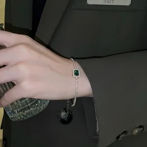 Elegant emerald square zircon bracelet with silver chain worn on a wrist over a blazer