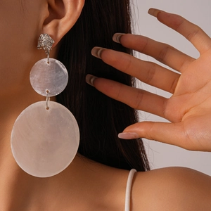 Close-up of oversized white shell-style earrings on model for a beach vacation look
