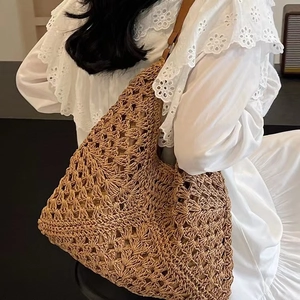 Dettaglio della borsa tote in paglia intrecciata con manico in pelle marrone sulla spalla