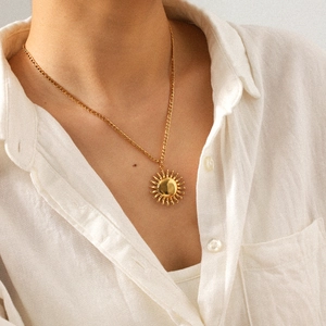 Gros plan d'un collier pendentif soleil en or 18k porté sur une chemise blanche pour femme