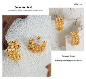 Detail of C-shaped gold beaded earrings featuring hollow metal spheres on a stone surface